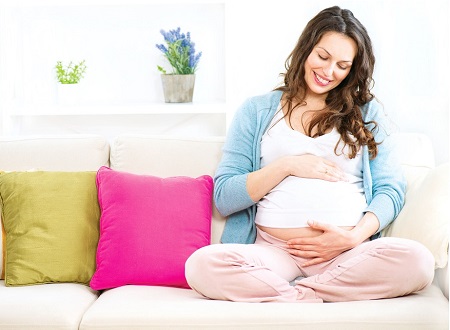 Счастливая беременная женщина на 9 месяце сидит на светлом диване